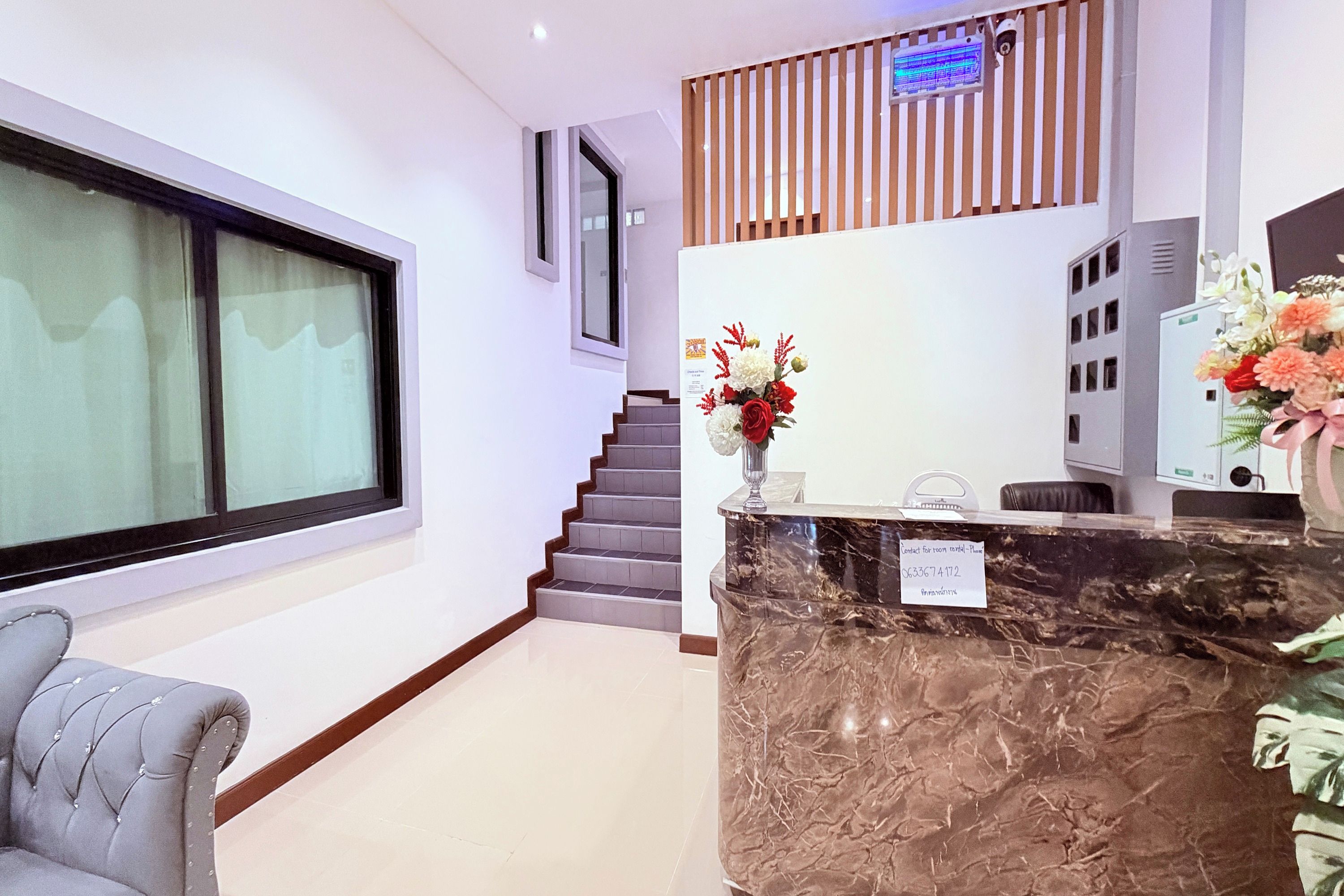 A hotel reception area with a marble counter, a grey upholstered chair, a staircase, and a large window.