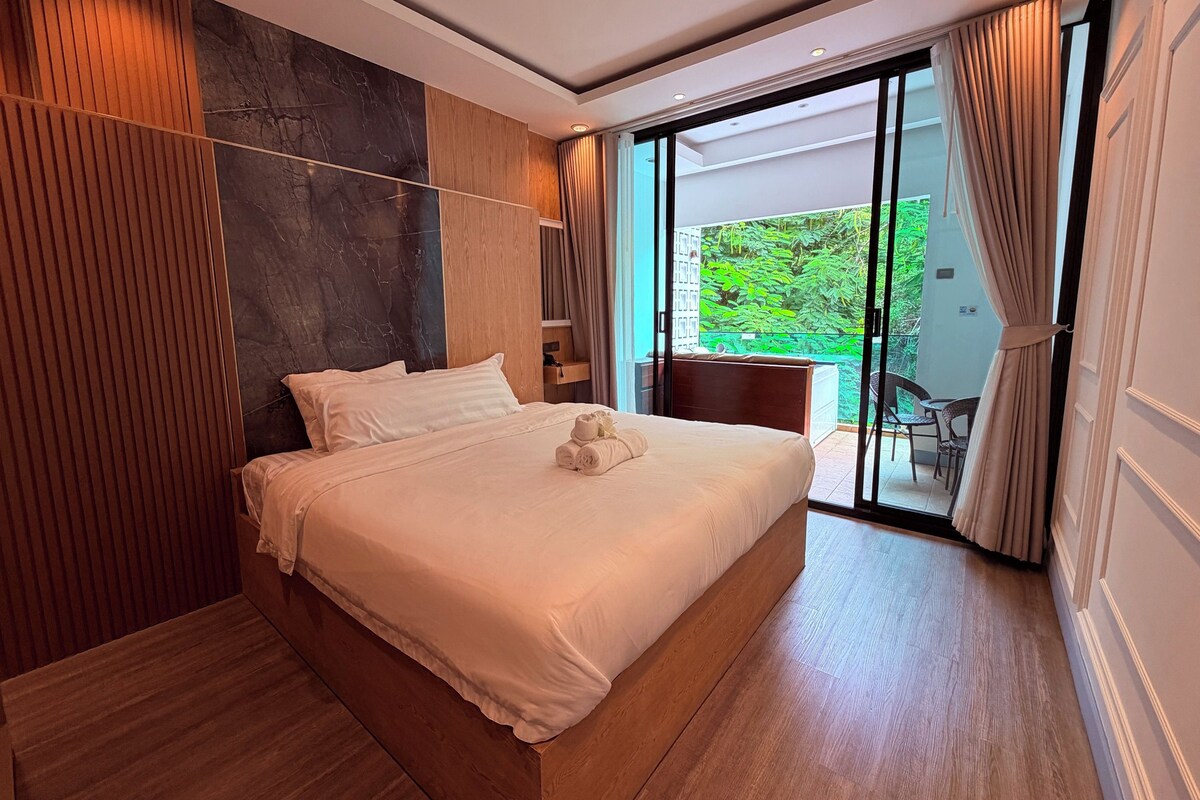 A modern bedroom with a large bed, wooden paneling, and a sliding glass door leading to a balcony.
