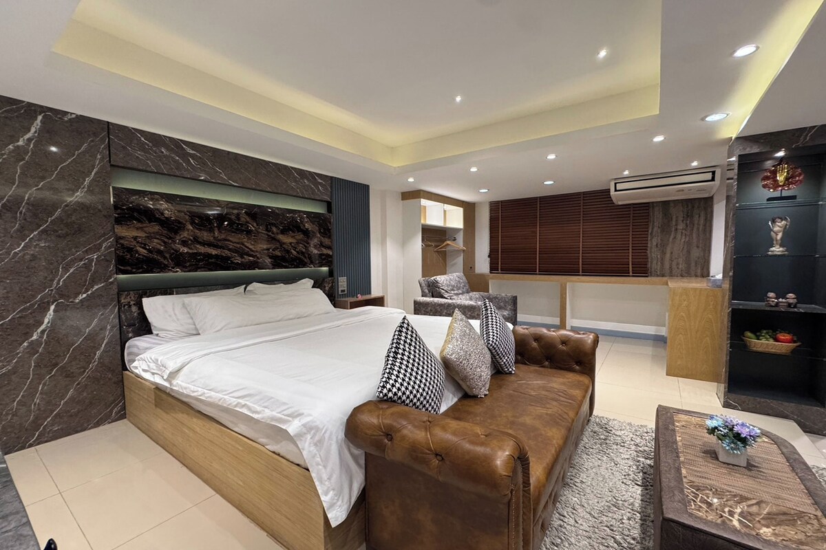A modern bedroom with a large bed, a leather sofa, and a small table with a vase.