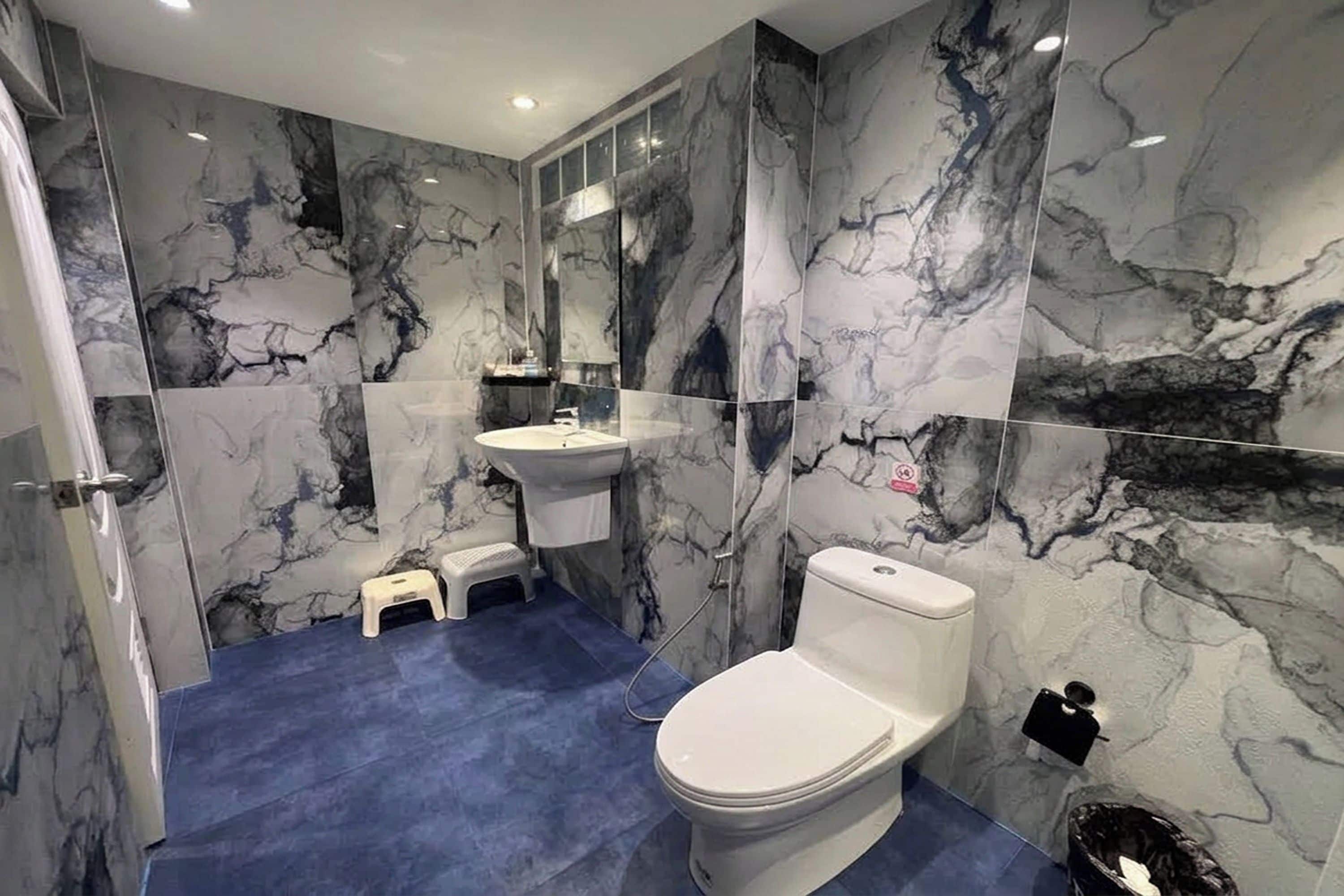 A bathroom with a marble wall, a sink, a toilet, and a small step stool.