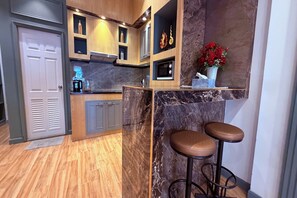 A modern kitchen with wooden cabinets, a marble countertop, and two bar stools. - M&M Rooftop Pattaya (Pattaya)