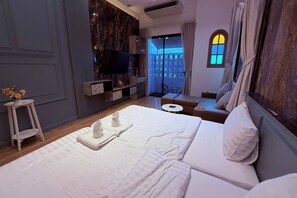 Habitació d'hotel amb llit, televisió, taula petita, sofà i finestra amb cortines.