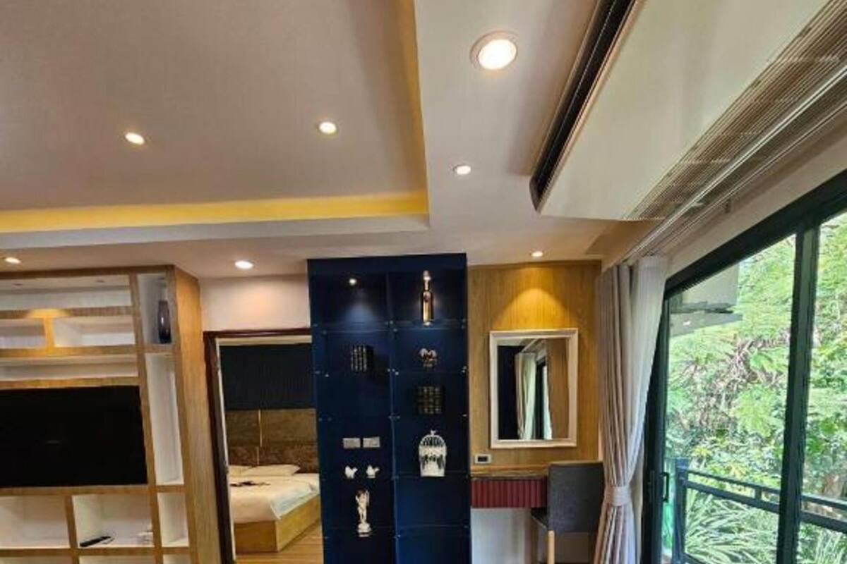 Ein modernes Hotelzimmer mit großem Fenster, einem Bett, einer Sitzecke mit kleinem Tisch und einem Schrank mit Spiegel.