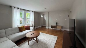 Un salon moderne comprenant un canapé, une table basse ronde en bois, un téléviseur et une petite table d’appoint avec une plante.