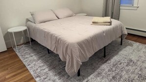 Un lit recouvert d’une courtepointe blanche, une petite table ronde et une fenêtre avec des stores.