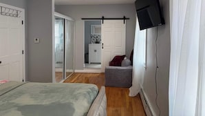 Ett sovrum med en säng, en tv som är monterad på väggen, en skjutdörr som leder till ett badrum och en liten sittgrupp.