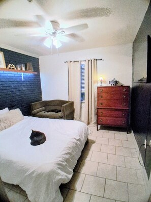 A bedroom with a bed, a dresser, a chair, a ceiling fan, and a window with curtains. - Quiet 2 Bedroom Boutique Style Apt in the Heart of Mid City Baton Rouge  (Baton Rouge)