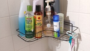 Un estante en el baño con varios artículos de aseo personal, incluyendo una botella de aceite de oliva, un producto para el crecimiento del cabello, un exfoliante corporal y una botella de champú.