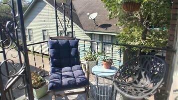 A balcony with a blue cushioned chair, a metal table, and potted plants.