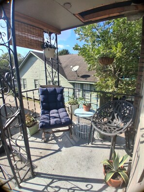 A balcony with a blue cushioned chair, a metal table, and potted plants. - Quiet 2 Bedroom Boutique Style Apt in the Heart of Mid City Baton Rouge  (Baton Rouge)