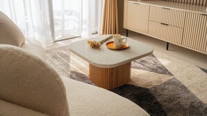 Moderni olohuone, jossa on sohva, sohvapöytä, jolla on kuppi ja kasvi, televisio puukehikon päällä ja läpikuultavat verhot.