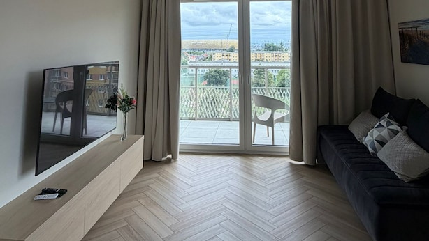 Un salon moderne avec un téléviseur, un canapé et un balcon offrant une vue sur la ville.