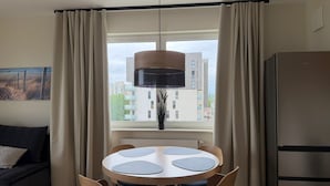Une cuisine moderne avec une table à manger, des chaises, un luminaire suspendu et une vue sur les bâtiments par la fenêtre.