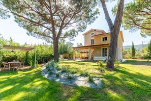 A two-story house with a patio, a garden with a stone pathway, and a pergola. - Design Villa La Vela - Goelba (Capoliveri)