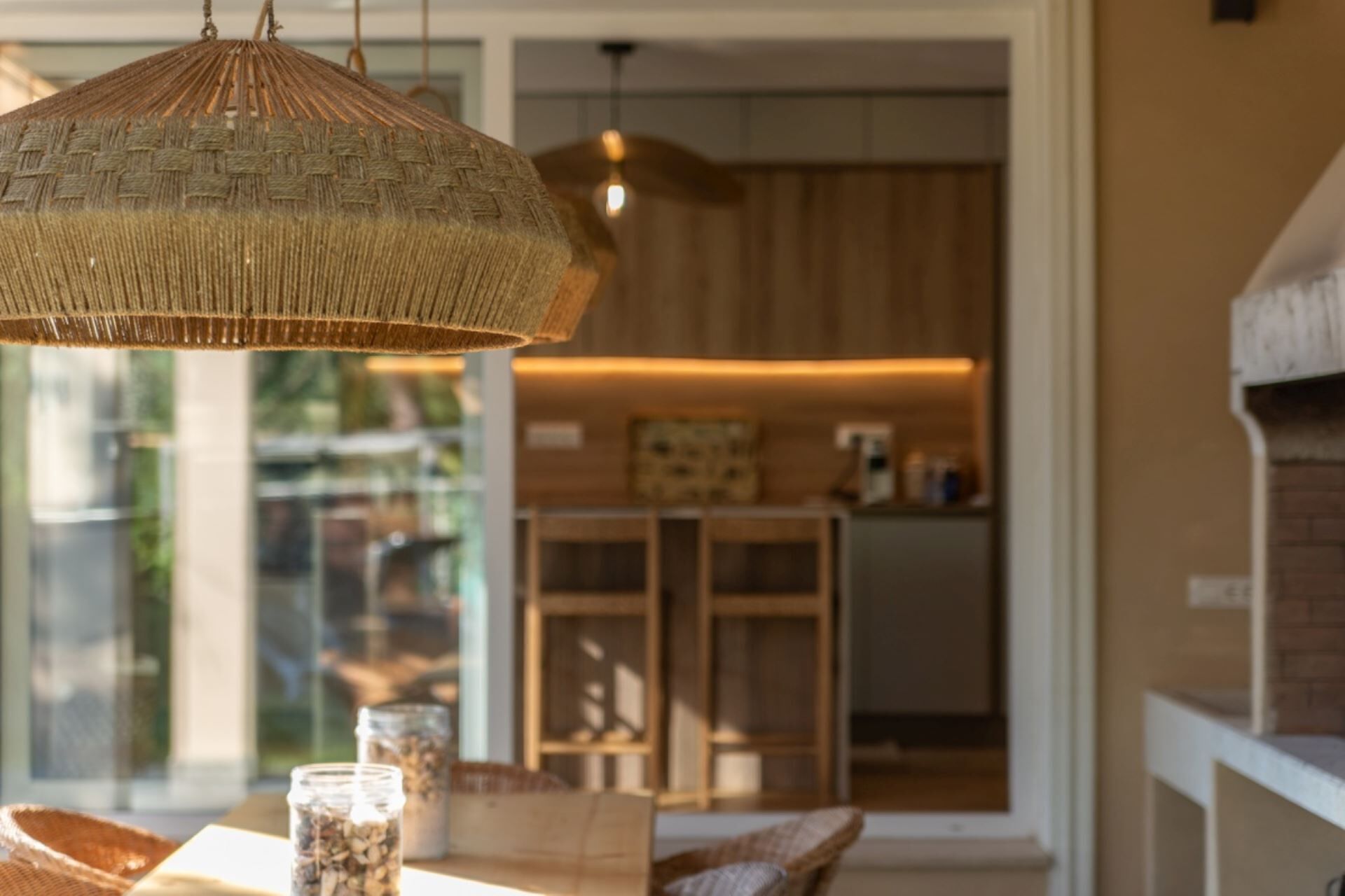 A dining area with wicker pendant lighting, a wooden table, and a view into a kitchen area.