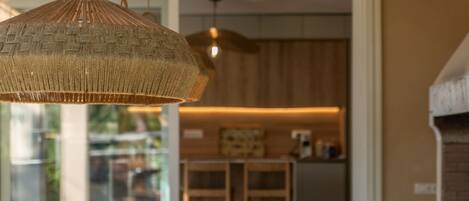A dining area with wicker pendant lighting, a wooden table, and a view into a kitchen area.