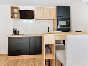 A compact kitchen with wooden cabinets, a black refrigerator, a microwave, and a coffee maker. - Dalmatica by Interhome (Kaštela)