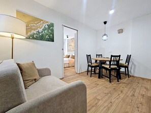 Ein Wohnzimmer mit einer Couch, einem Esstisch mit Stühlen, einer Lampe und einem Bild an der Wand.