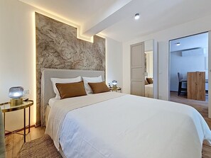 Ein modernes Schlafzimmer mit einem großen Bett, einer Wand mit Marmorverkleidung, einem Nachttisch mit Lampe und einem Holztisch.