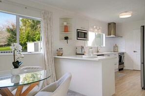 A modern kitchen with a glass dining table, white cabinetry, and a view of the outdoors.