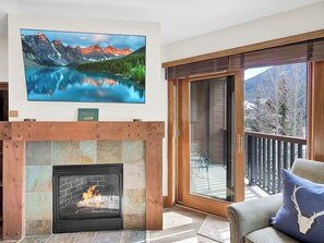 A living room with a fireplace, a television mounted on the wall, and a balcony with a view of the mountains. - The Springs at River Run - Walk to Gondola - Pool w/ Slide - Hot Tubs - Sleeps 4 (Keystone)