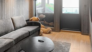 Ett modernt vardagsrum med en grå soffa, ett runt soffbord och ett stort fönster med utsikt över en byggnad och träd.