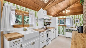 Een keuken met witte kasten, houten aanrecht, een inbouwoven en een raam met uitzicht op groen.