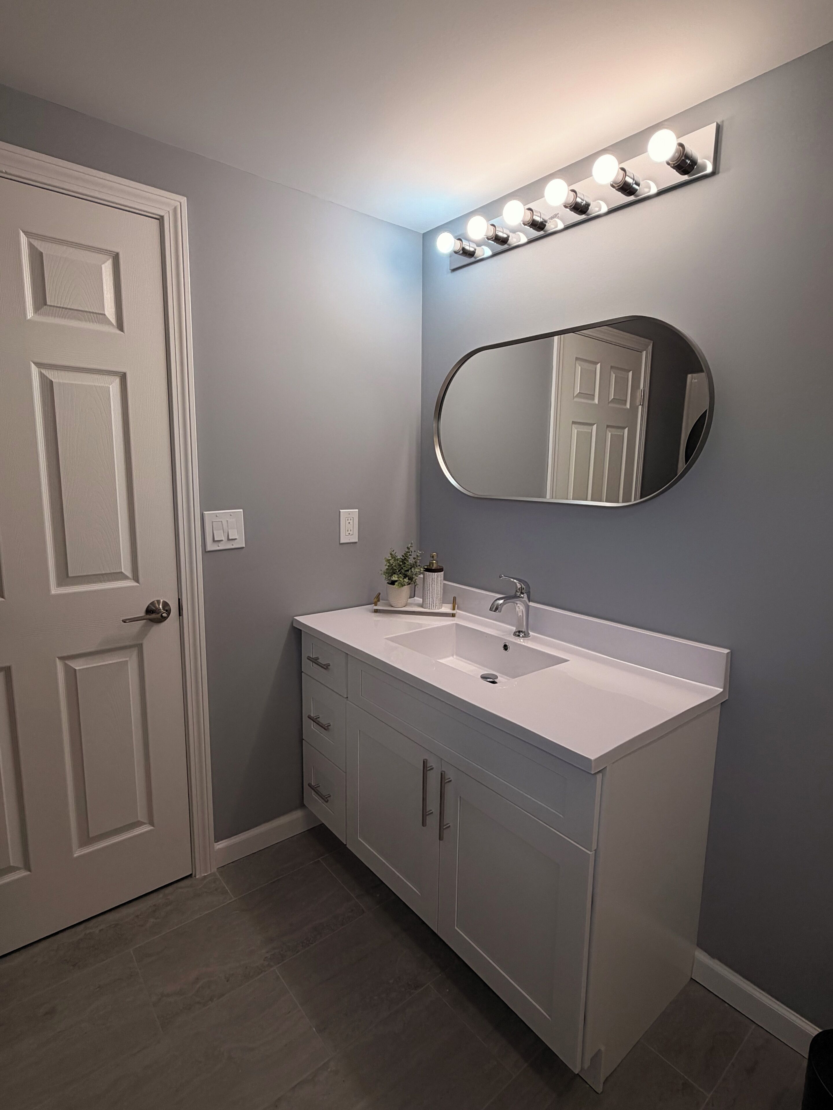 A bathroom with a white vanity, a large mirror, and a lighted vanity mirror.