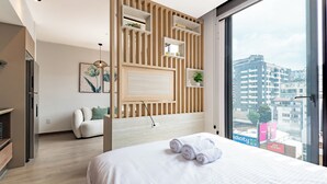A modern hotel room with a large bed, a wooden accent wall, a view of the city, and a small balcony. - Edificio SEIS by Host Ecuador (Quito)