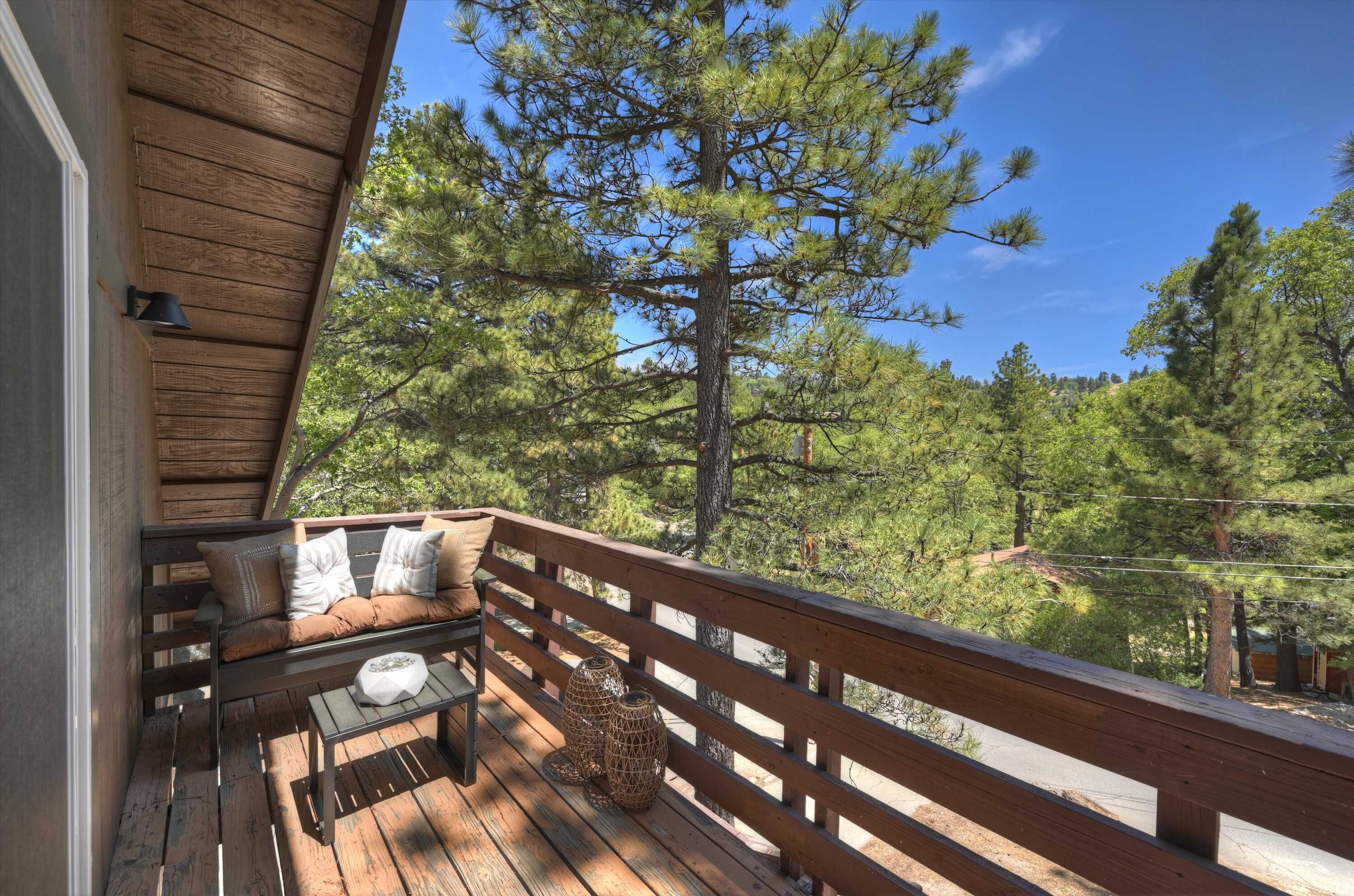 A wooden deck with a bench and table, surrounded by trees.