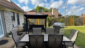 Un pati exterior amb una taula i cadires, una barbacoa i una zona de seients coberta.