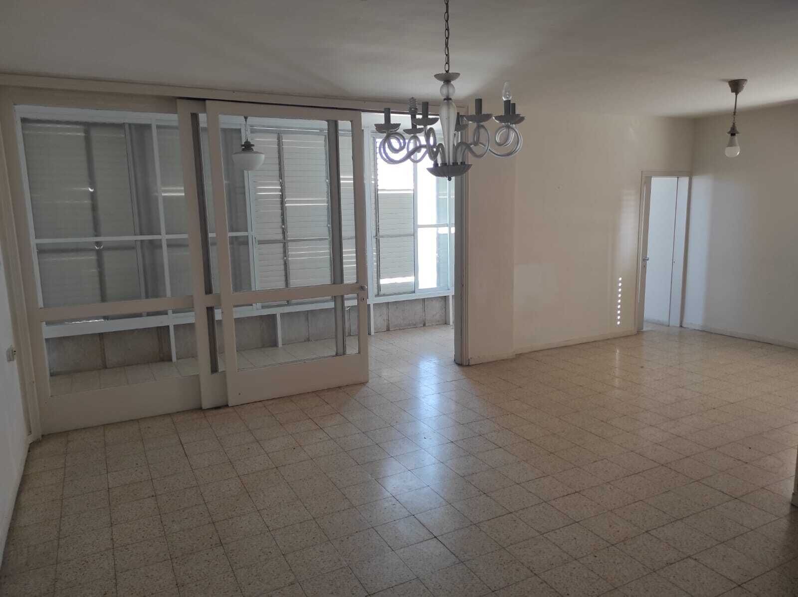 A spacious room with a large sliding glass door, a chandelier, and tiled flooring.