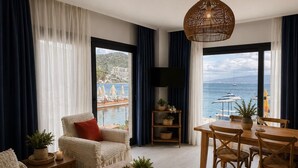 A modern living room with a sofa, a wooden coffee table, a dining table with chairs, a TV, and a view of the sea. - Moonlight Pansiyon (Akyarlar)