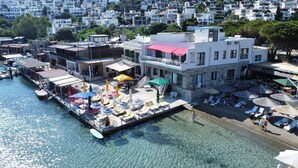 A waterfront property with a pool, lounge chairs, and umbrellas. - Moonlight Pansiyon (Akyarlar)