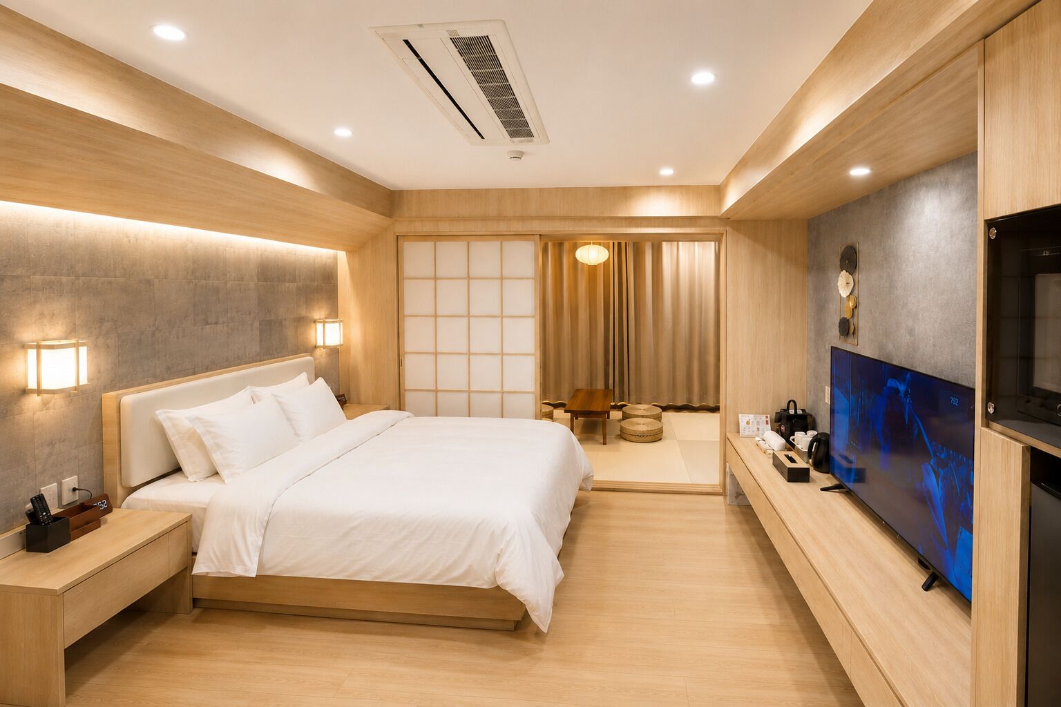 A modern hotel room with a large bed, bedside tables, a flat-screen TV, and a sliding door leading to a bathroom.
