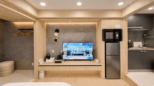 A modern hotel room with a flat-screen TV, a refrigerator, a kitchen area, and a seating area with a small table and chairs. - BACOWA AWAZA (Nishi-ku, Osaka)