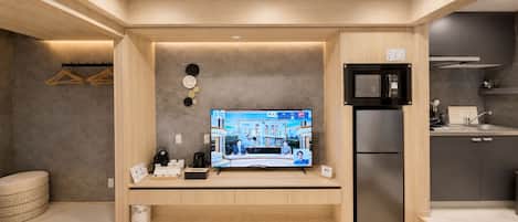 A modern hotel room with a flat-screen TV, a refrigerator, a kitchen area, and a seating area with a small table and chairs.