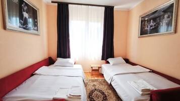 Een hotelkamer met twee bedden, een kleine tafel en een raam met gordijnen.