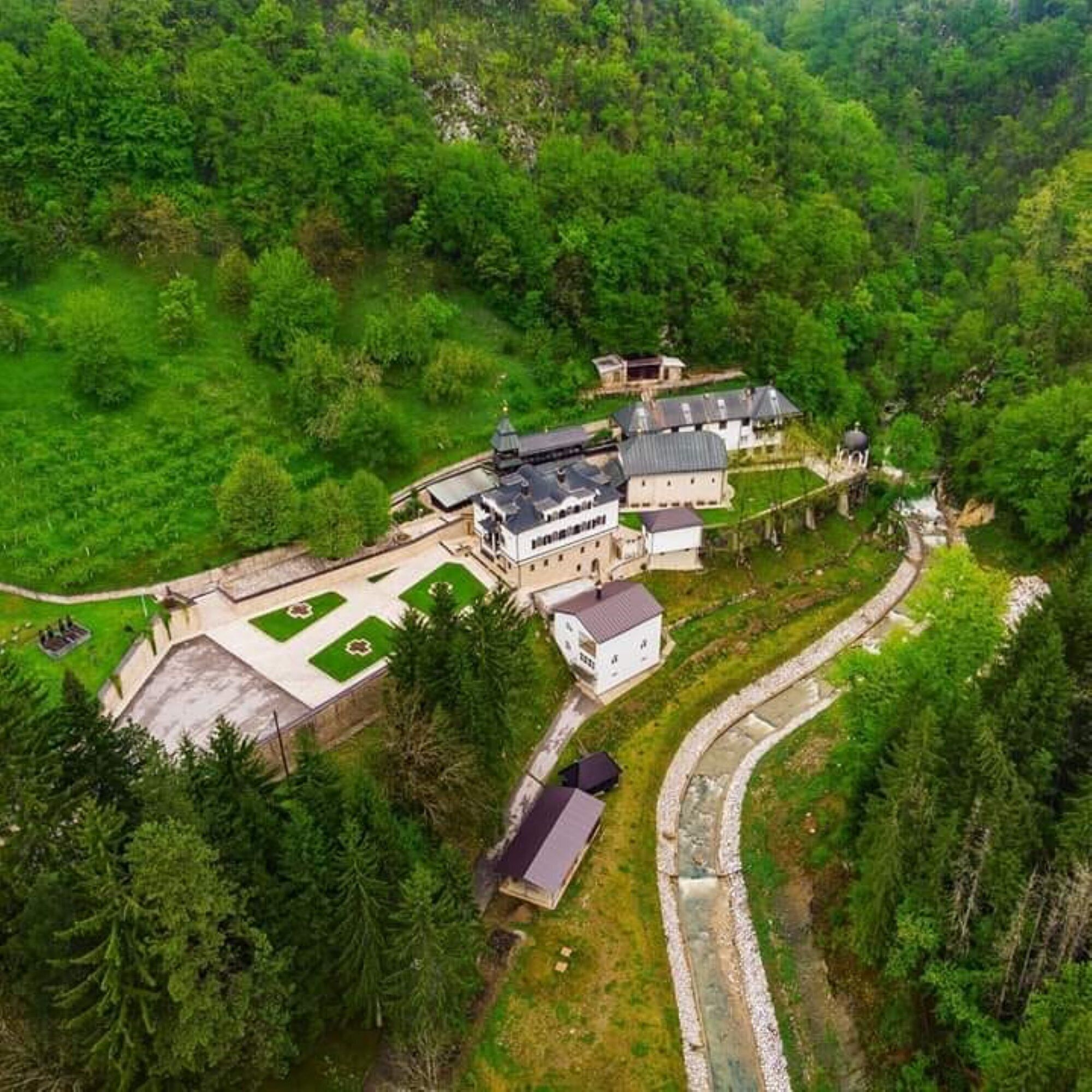 An aerial view of a large estate with multiple buildings, a tennis court, and a winding pathway.