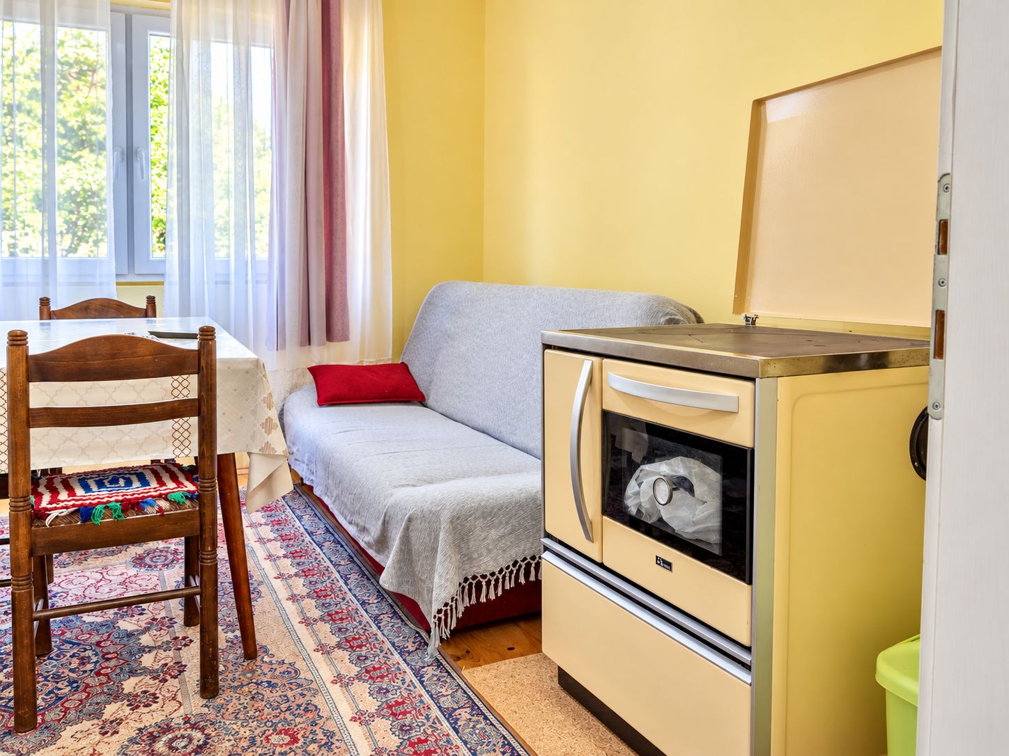 Una habitación compacta con sofá, una mesa de comedor con sillas, una pequeña kitchenette con refrigerador y una alfombra estampada.