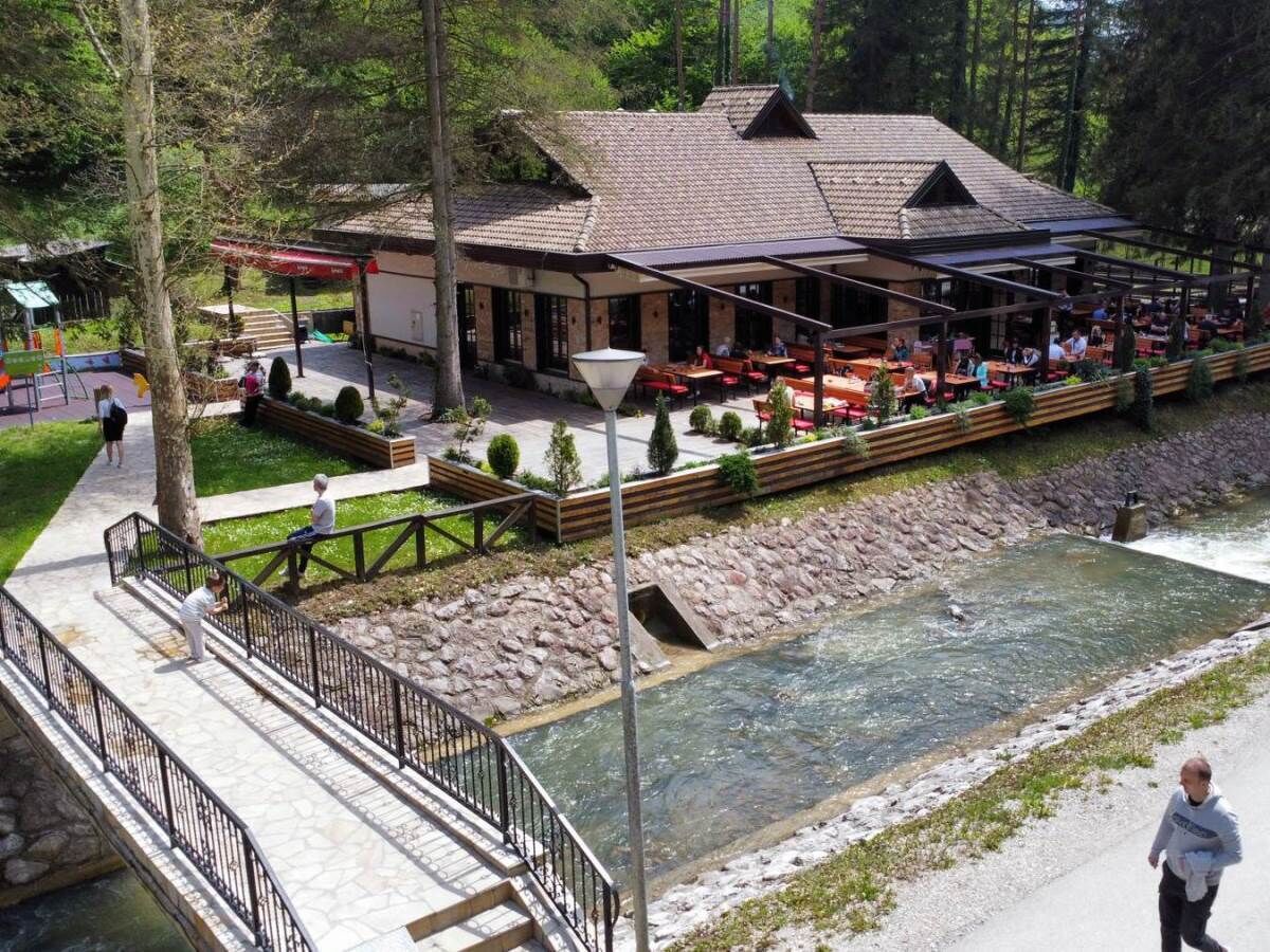 A riverside restaurant with outdoor seating, a stone pathway, and a wooden deck.