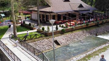 A riverside restaurant with outdoor seating, a stone pathway, and a wooden deck.