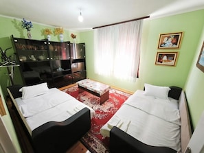 Una habitación con dos camas, una mesita, un televisor y un armario.