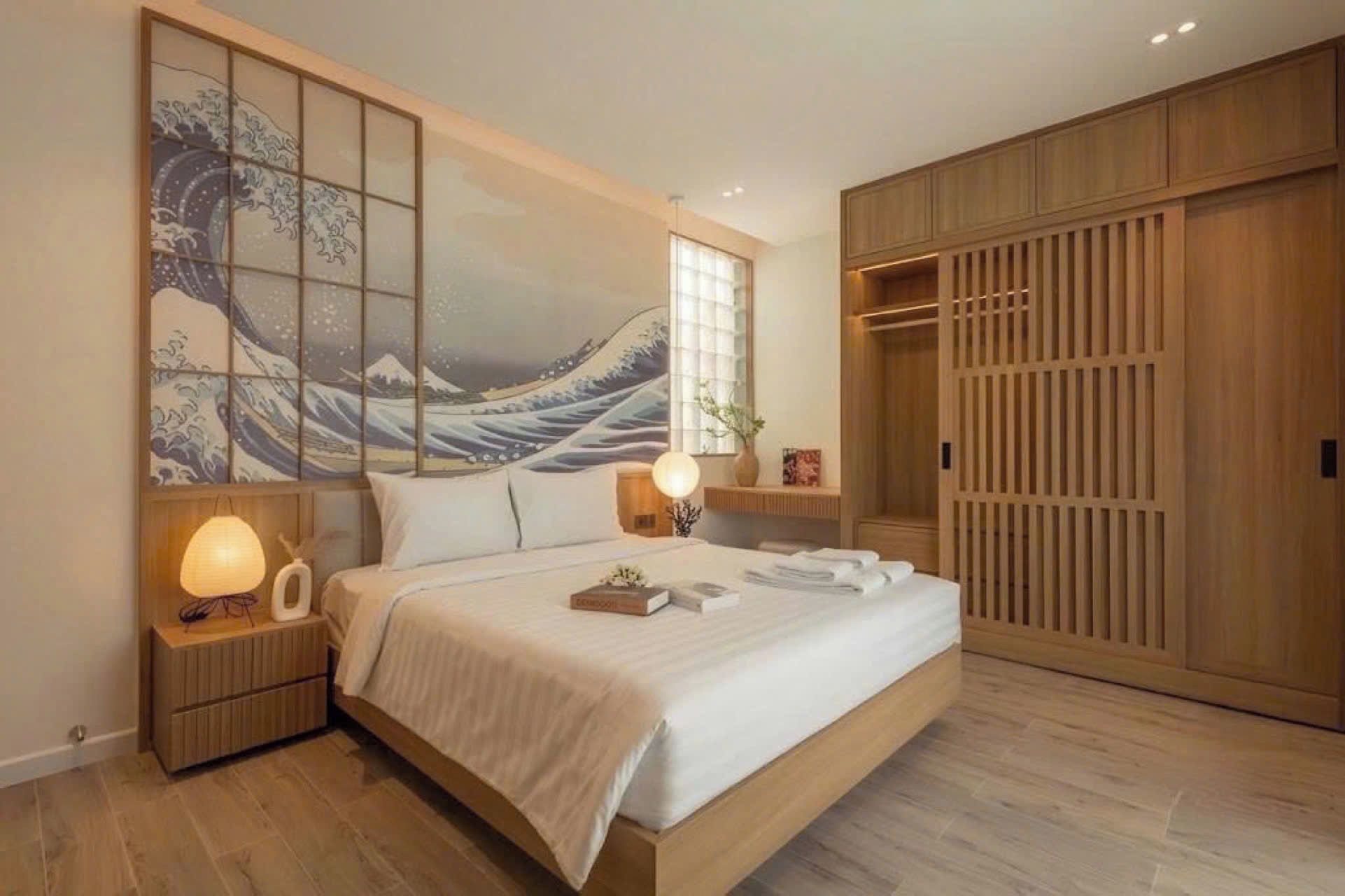 A bedroom with a large bed, a shoji screen, a wooden wardrobe, and a nightstand with a lamp.