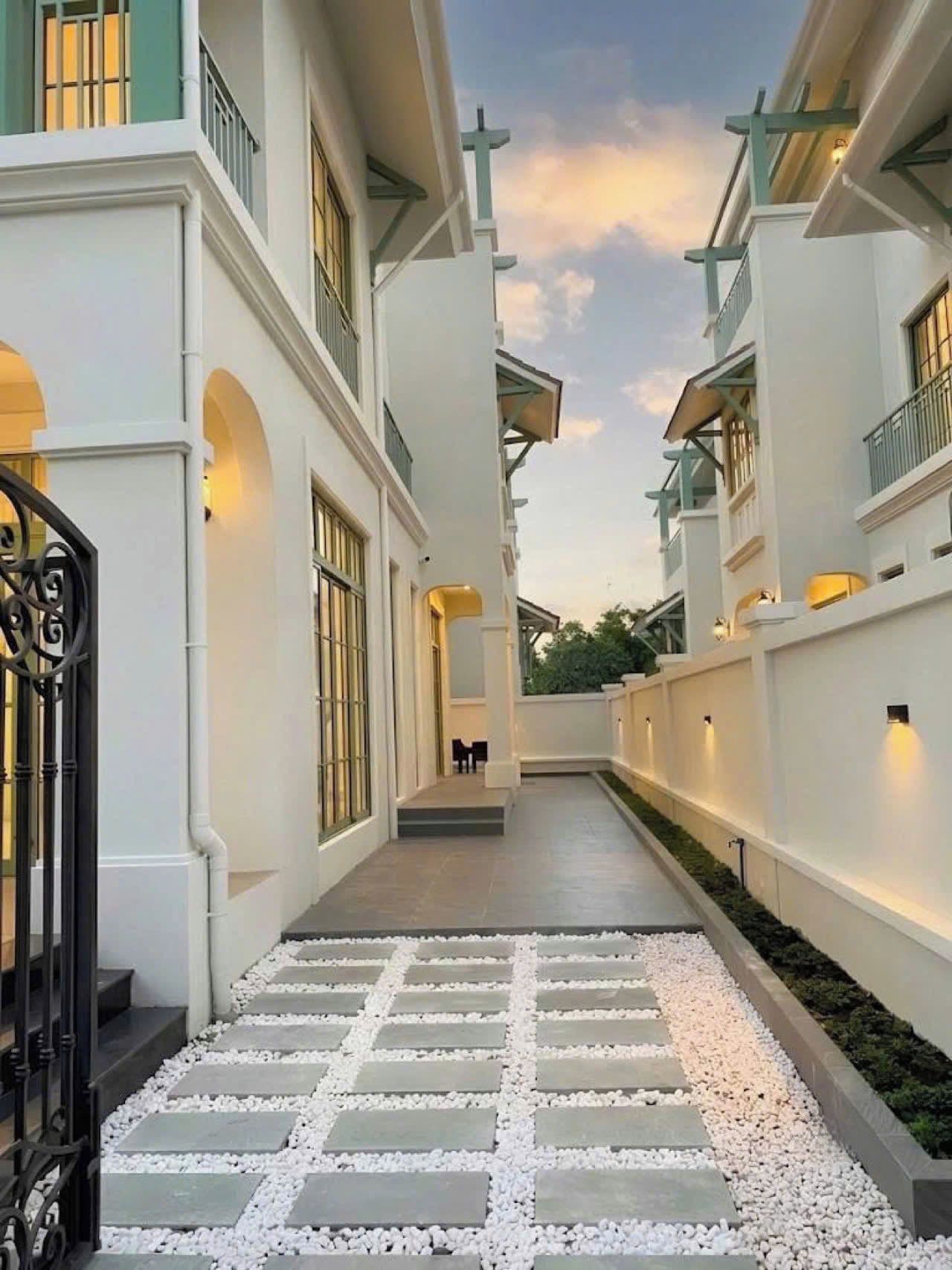A corridor with a stone pathway leading to a seating area, flanked by white walls and balconies.