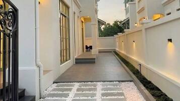 A corridor with a stone pathway leading to a seating area, flanked by white walls and balconies.