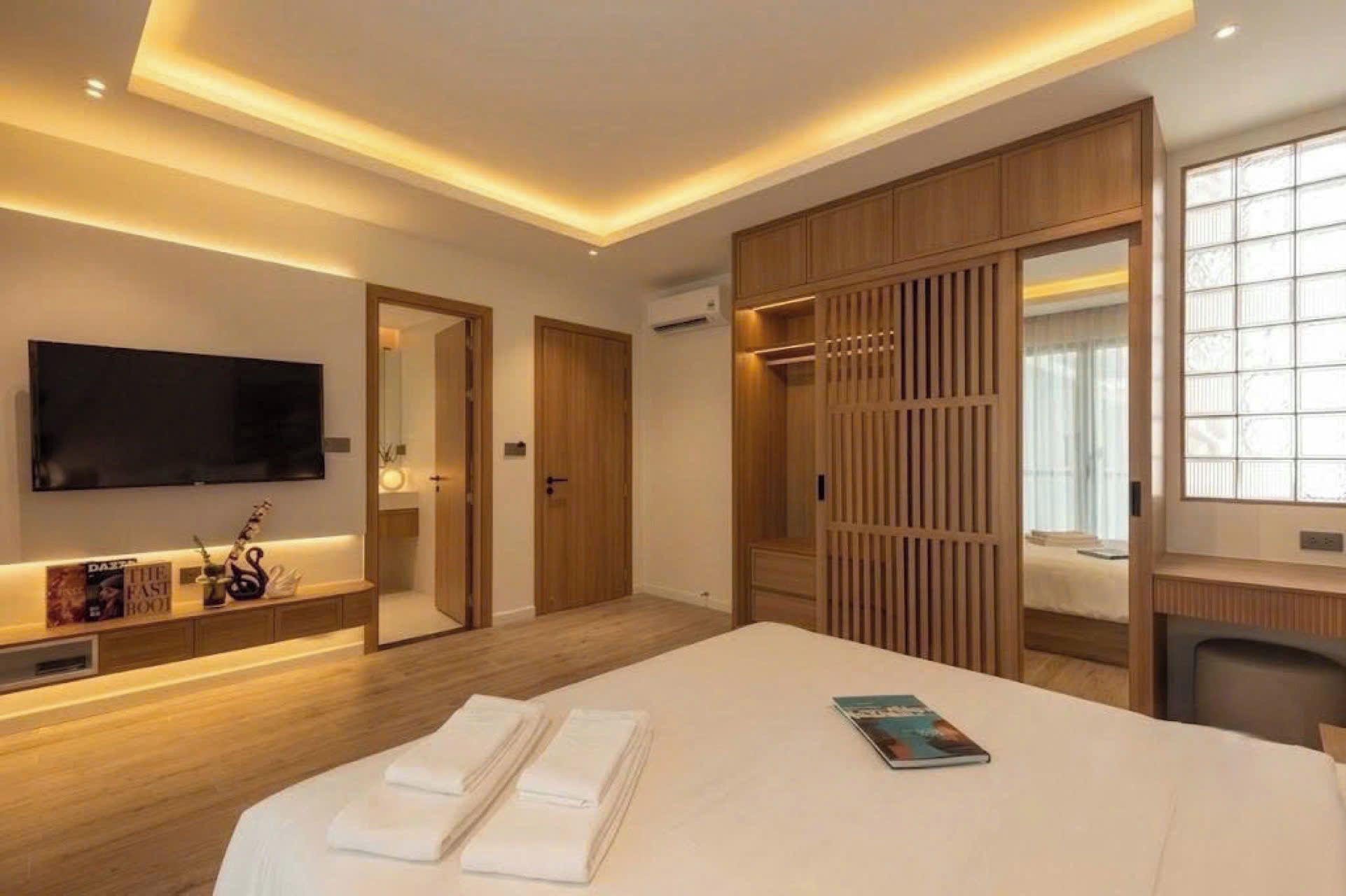 Ein Hotelzimmer mit einem großen Bett, einem wandmontierten Flachbildfernseher, einem Holzschrank und einem Nachttisch mit einer Zeitschrift.