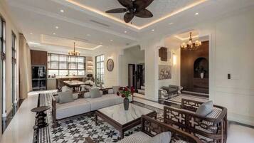 A spacious living room with a high ceiling, a central seating area with sofas and a coffee table, and a kitchen area in the background.