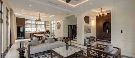 A spacious living room with a high ceiling, a central seating area with sofas and a coffee table, and a kitchen area in the background.