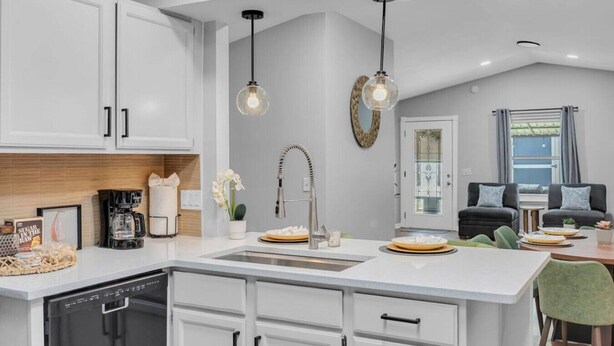 Una cucina moderna con mobili bianchi, un'isola centrale, luci a sospensione e un'area pranzo con sedie verdi.